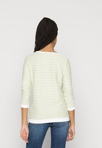 Haut à manches longues rayé vert et blanc avec un col rond et une coupe décontractée. Caractéristiques : bords roulés aux manches et à l'ourlet. Porté avec un jean bleu.