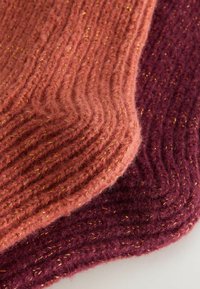 Strickstoff in warmem Pink und tiefem Burgunderrot, mit einer wellenförmigen Textur und goldenen Metallfäden, die durchgewebt sind.