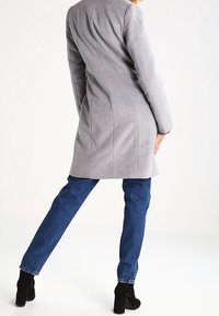 Abrigo gris de mezcla de lana con costuras en la espalda, textura suave, mangas largas, combinado con vaqueros azules y botines de ante negros.