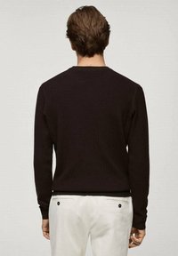 Dunkelbrauner, gerippter Pullover mit rundem Halsausschnitt, langen Ärmeln und taillierter Silhouette, kombiniert mit hellen Hosen.