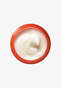Crème blanche dans un contenant rond avec une texture lisse et un couvercle orange vif. La crème présente un motif en spirale circulaire sur le dessus.