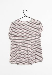 Kevätkukkakuvioinen lyhythihainen paita kevyessä valkoisessa kankaassa, jossa on smokkivarsi. Kuosissa on pieniä viininpunaisia ja vihreitä kukkia. Ripustettuna mustaan koukkuun.