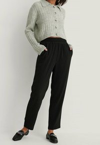 Jasnoszary sweter prążkowany z kołnierzykiem, z guzikami z przodu, zestawiony z czarnymi spodniami w prążki, z elastycznym pasem.