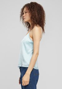 Camisolă din satin de culoare albastru deschis, cu bretele subțiri, croială lejeră și textură netedă, asortată cu blugi din denim cu talie înaltă.