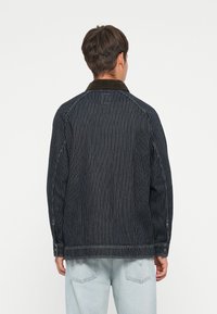 Striped denim jacket in dark blue with a brown corduroy collar, featuring buttoned cuffs and visible stitching detail.