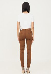 Ciemnobrązowe skinny jeansy z wysokim stanem, tylnymi kieszeniami i przeszyciami, w połączeniu z prostą białą koszulką oraz szpilkami w wężowy wzór.