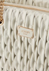 Prešívaná krémová kožená kabelka so zlatými doplnkami, s obdĺžnikovou visačkou značky "JOOP! JEANS" a detaily z pleteného reťazca.