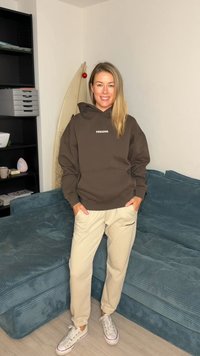 Brown hoodie with "PECADOR" logo, soft fabric, and large hood, paired with light beige joggers. White sneakers complete the outfit.