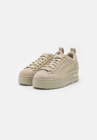 Sneaker in suede beige con suole a piattaforma spessa, punta arrotondata e allacciatura frontale. Presenta dettagli in cucitura e un logo sul lato.
