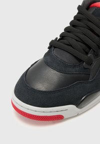 Schwarze Wildleder- und Leder-Sneaker mit strukturiertem Finish, ausgestattet mit schwarzen Schnürsenkeln, roten Akzenten an der Sohle und einem gepolsterten Knöchelbereich.