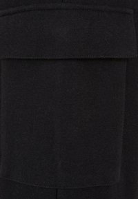 Gros plan d'une poche en tissu noir avec un rabat cousu sur un vêtement, montrant la texture et les détails de la couture.