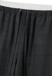 Zwart geblokt stof met een elastische witte tailleband en zilveren oogjes voor de trekkoord. Het materiaal heeft een zachte, gestructureerde afwerking.