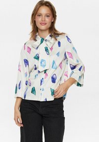 Camicia bianca con motivi di cristallo colorati in blu, verde, rosa e viola. Presenta un colletto a fiocco e maniche a tre quarti.