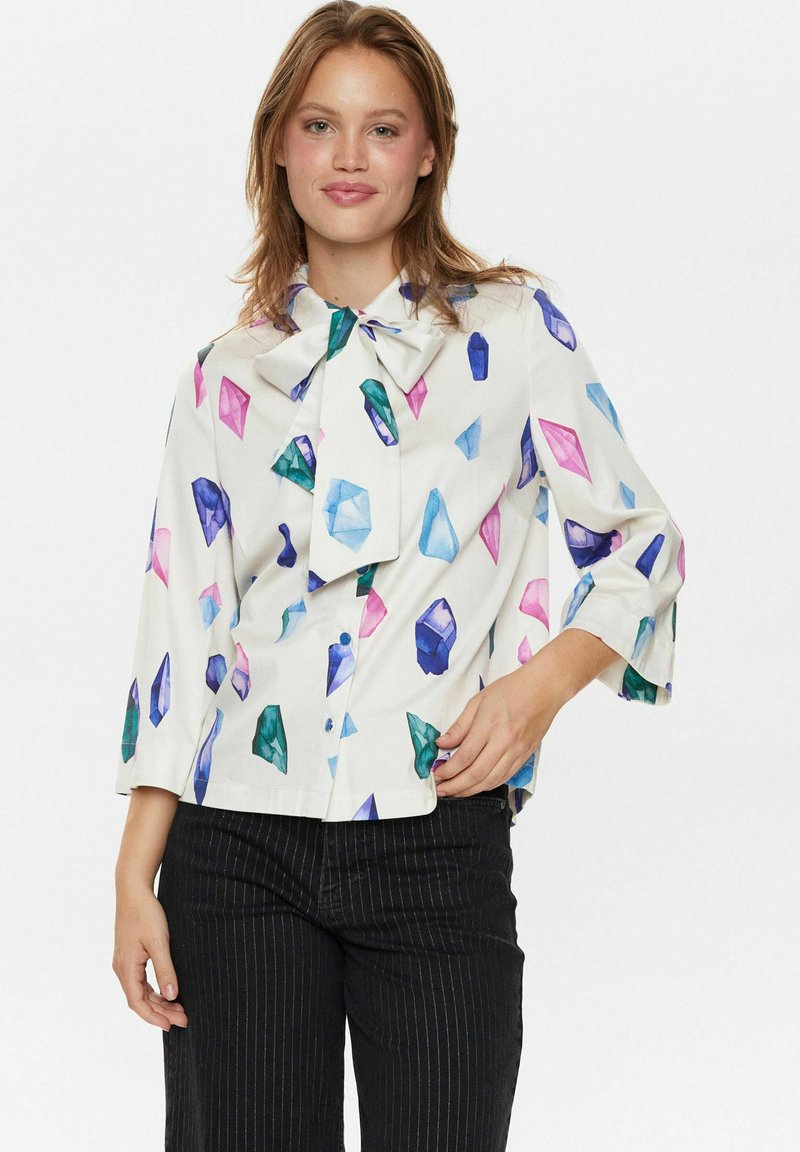Camicia bianca con motivi di cristallo colorati in blu, verde, rosa e viola. Presenta un colletto a fiocco e maniche a tre quarti.