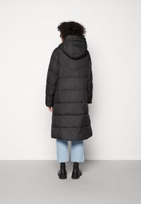 Sort lang pufferjakke med hætte, lodret stikningsmønster og lige snit, parret med lys blå cropped jeans og sorte støvler.