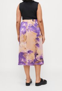 Personne portant une jupe midi tie-dye violette et beige, un haut noir sans manches et des chaussures noires épaisses à brides, vue de dos.