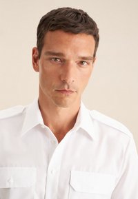 Witte blouse met een puntkraag, korte mouwen en twee borstzakken. Glad stof met een frisse afwerking en zonder zichtbare patronen.