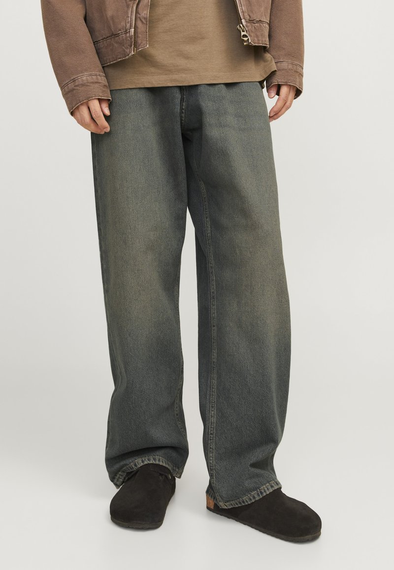 Wide-leg jeans in a faded blue-gray denim with a smooth texture. Worn with a brown top and black slip-on shoes.