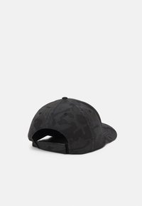 Gorra de béisbol con patrón de camuflaje negro vista desde atrás, con correa ajustable y ojetes de ventilación sobre un fondo liso.