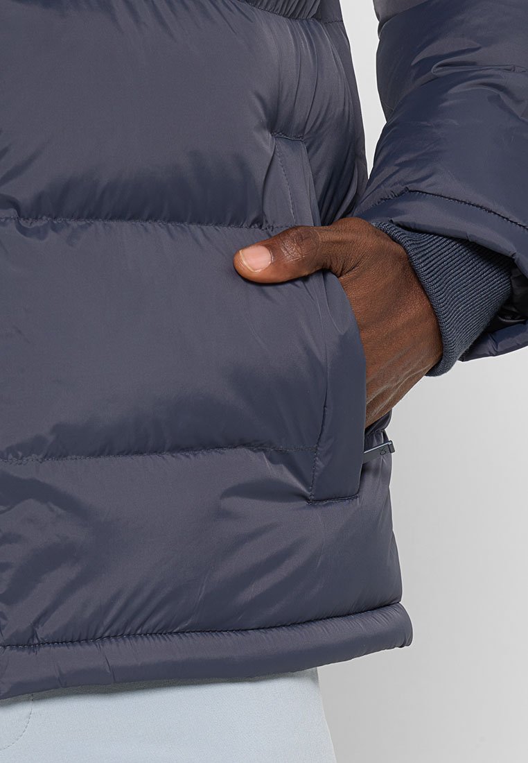 Blouson matelassé bleu marine avec design matelassé, doté d'une poche latérale, de poignets côtelés et d'une texture lisse. Rembourrage pour la chaleur.