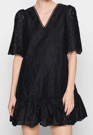 Černé krátké šaty s nabíranými rukávy, výstřihem do V, výšivkou s dírkami a volánkovým lemem sahajícím do poloviny stehna na osobě s odhalenýma nohama.