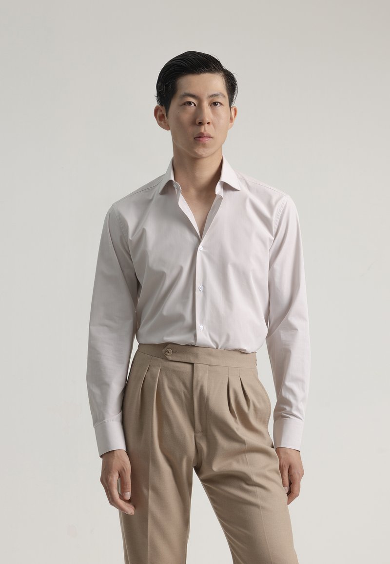 Camisa de vestir blanca a rayas con cuello abotonado, combinada con pantalones de tiro alto beige con pliegues y un detalle de botón circular.