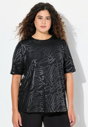 Zwarte top met korte mouwen met een glanzend, textuurpatroon van grote zwarte pailletten; ronde halslijn en een losse pasvorm, gecombineerd met zwarte broek.