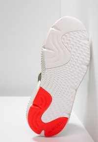 Sula i texturerad vit gummi, med en framträdande röd accent och ett vågigt mönster för grepp. Logotyp i röd färg synlig på sulan.