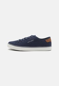 Marineblaue Segeltuch-Sneaker mit weißen Gummisohlen, passenden Schnürsenkeln, einem braunen Lederakzent an der Ferse und minimalistischen Designdetails.