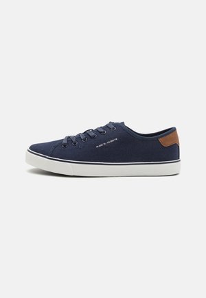Zapatillas de lona azul marino con suelas de goma blanca, con cordones coordinados, un detalle de cuero marrón en el talón y un diseño minimalista.