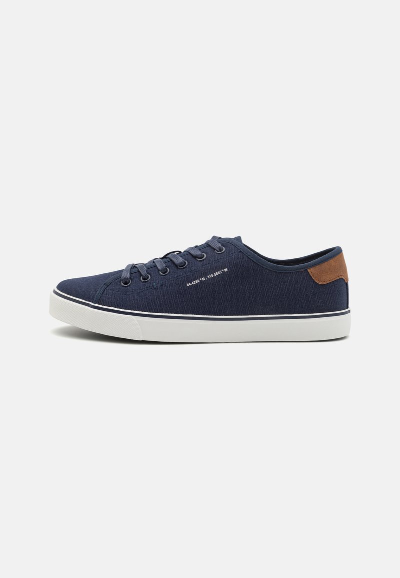 Marineblaue Segeltuch-Sneaker mit weißen Gummisohlen, passenden Schnürsenkeln, einem braunen Lederakzent an der Ferse und minimalistischen Designdetails.