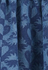 Tissu en denim avec une base bleu foncé présentant un motif texturé de feuilles et de cœurs en bleu clair, avec des plis verticaux.