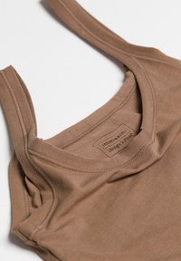 Brun ärmlös topp i mjukt tyg. Har en rund halsringning och en etikett med texten "Ultralight SUPIMA" sydd inuti.