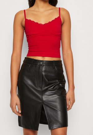 Mujer con top corto de tirantes finos con encaje rojo y falda negra de cuero hasta la rodilla con abertura frontal.