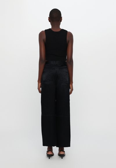 Zwarte cropped ribbed tanktop gecombineerd met hooggeknipte, loszittende zwarte culottes. Glad materiaal met een subtiele glans.