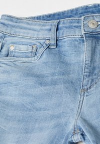 Vaaleansiniset denim-farkut, joissa on klassinen viiden taskun muotoilu, yksittäinen nappisulku ja hienovarainen haalistuminen kankaan päällä luomaan tekstuuria.