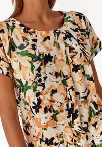 Blusa floreale in tessuto leggero. Presenta un collo a giro, maniche corte e un motivo floreale multicolore in arancione, verde e nero.