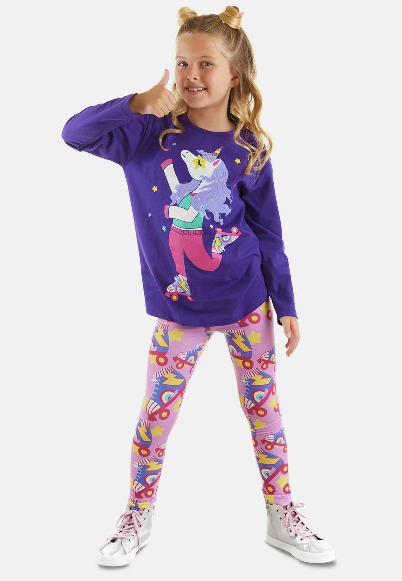 Paarse longsleeve shirt met een eenhoornafbeelding, gecombineerd met roze leggings met een kleurrijk rolschaatsenpatroon, afgewerkt met zilveren sneakers.