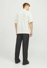 Korte mouw, off-white gebreid shirt met verticale ribbelstructuur, gecombineerd met zwarte wijde broek en zwarte schoenen.