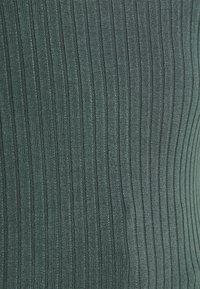 Tummanvihreä ribbeerikangas yläosa, jossa on teksturoitu kuvio pystysuorilla viivoilla ja pehmeä, sileä pinta.