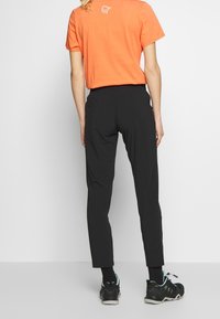 Svarta träningsbyxor med smal passform, elastisk midja och mjukt material. I kombination med en orange t-shirt med kort ärm och svarta sneakers.