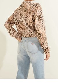 Blusa con estampado de leopardo, de manga larga, corte relajado, con puños elásticos, combinada con jeans de tiro alto en azul claro que cuentan con un parche triangular de logo.