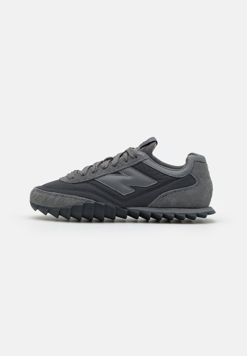 Baskets New Balance gris foncé avec des panneaux en suède et tissu, semelle à motif zigzag et fermeture lacée, vues de côté.