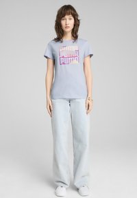 Svetle modré bavlněné tričko s grafickým designem, na kterém je slovo "Puma" v růžové a purpurové barvě. Vybavené s světle modrými širokými džíny.