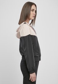 Lett og tettsittende hettejakke i rosa og svart. Glatt stoff med elastiske mansjetter og nederkant, med glidelås og kontrastfargede paneler.