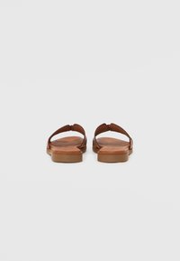 Brown sandals with a flat sole, thong design, and a smooth leather texture. Light brown footbed with subtle detailing.