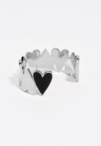 Anillo de plata con formas alternas de corazón y punta, con un destacado detalle de corazón negro y una textura metálica suave.