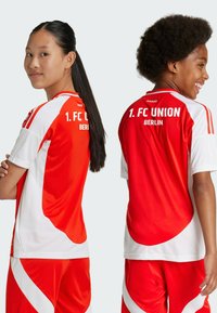 Maglie sportive rosse e bianche con texture a rete, con il testo "1. FC UNION BERLIN" sulla schiena. Pantaloni corti inclusi nello stesso design.