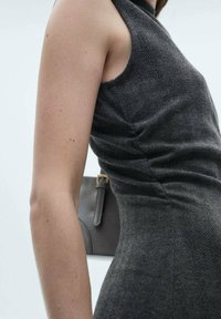 Rochie gri în model herringbone, cu o siluetă ajustată, fără mâneci și dintr-un material texturat. O geantă închisă este vizibilă în fundal.