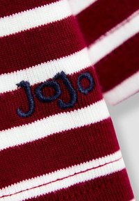 Burgundy ja valge triibuline kangas, millel on sinises värvis tikitud "JoJo" tekst. Sujuv tekstuur koos soonikute mansettidega, rõhutades värvi kontrasti.
